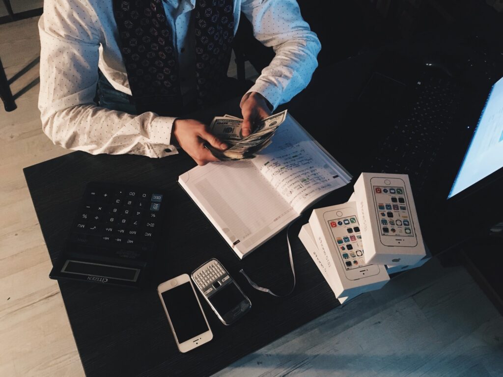 Canva-Person-Counting-Money-With-Smartphones-in-Front-on-Desk
