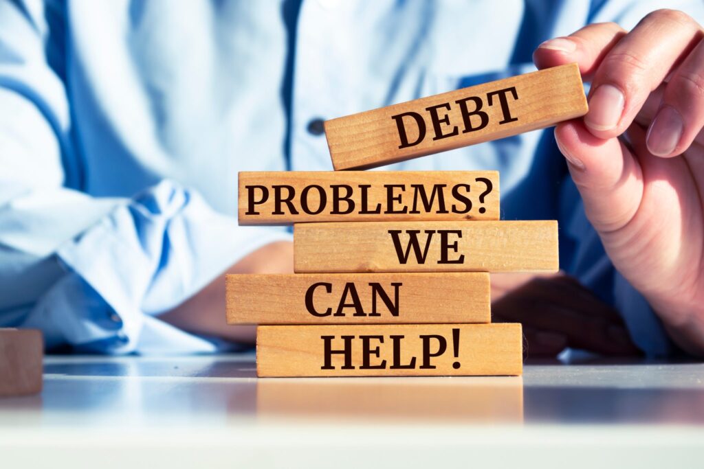 Person holding wooden block labeled 'Debt' above a stack of blocks reading 'Problems? We Can Help!